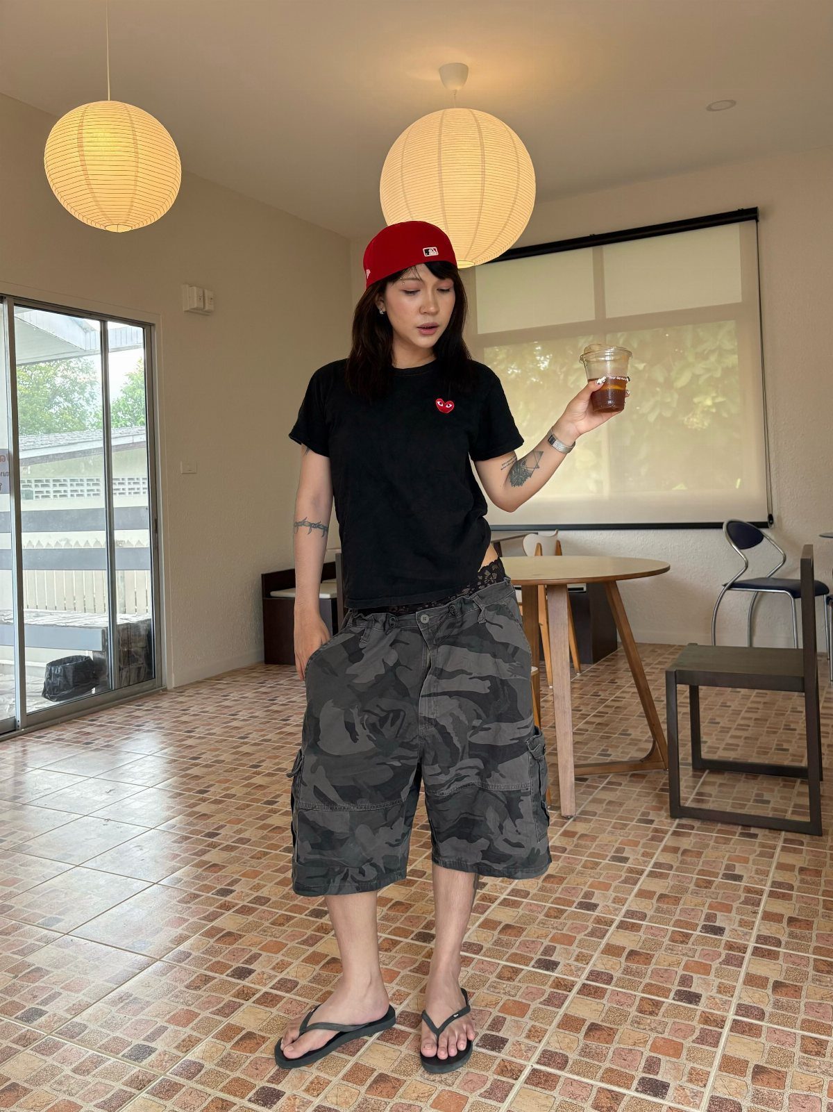 Woman in black t-shirt and grey camouflage cargo shorts standing in a room.
