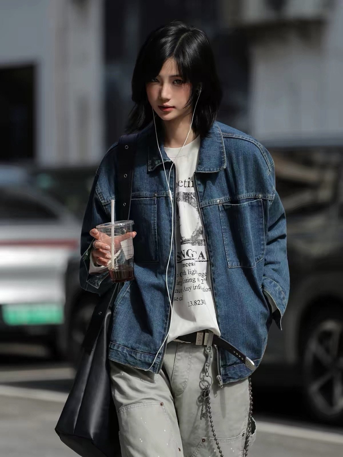 Young woman in an oversized denim jacket, graphic t-shirt, and grey cargo pants walking outdoors.