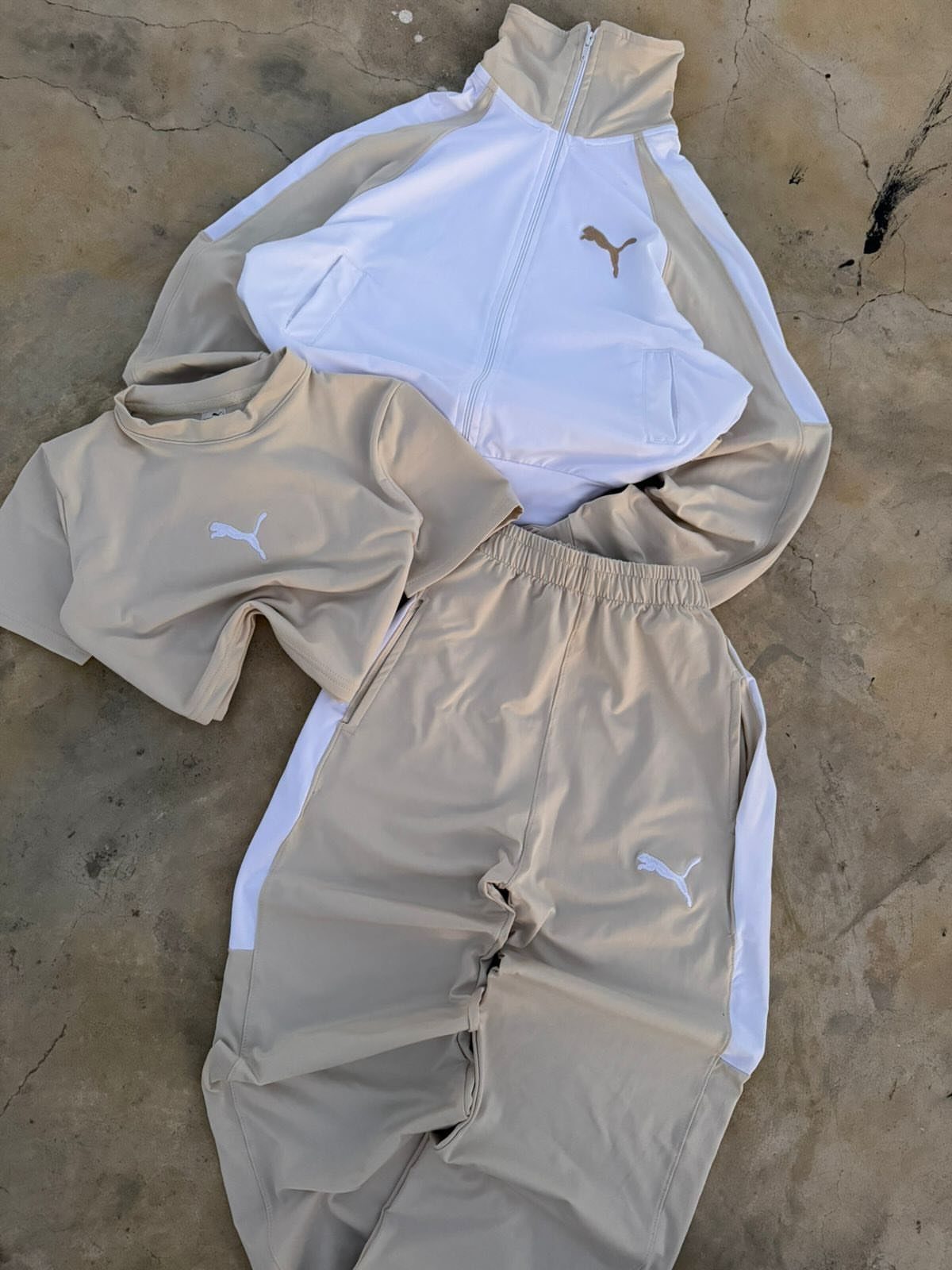 Beige and white Puma track jacket, t-shirt, and joggers laid on concrete.