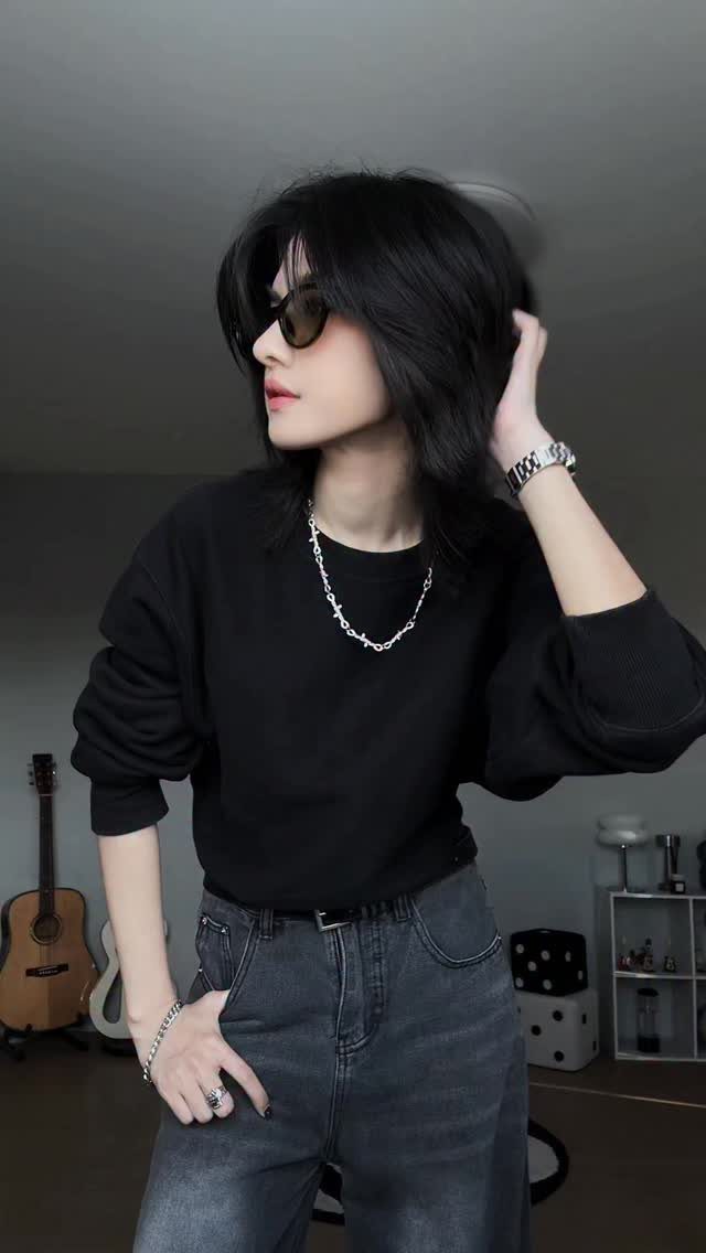 A person in a black sweatshirt, sunglasses, and dark jeans posing indoors.