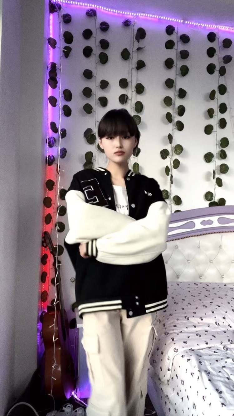 A person wearing a black and white varsity jacket and beige cargo pants standing indoors.