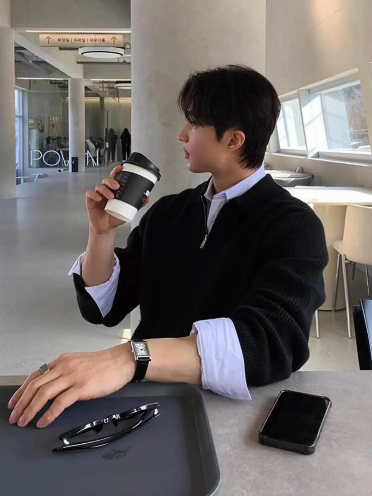 Young man in a black sweater and white collared shirt sitting at a cafe table.