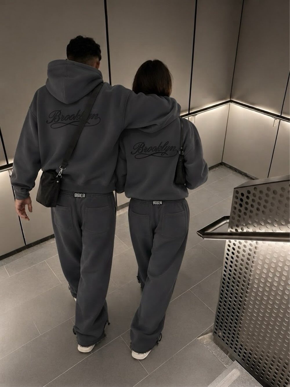 Two people walking up stairs wearing matching grey hooded sweatshirts and sweatpants.