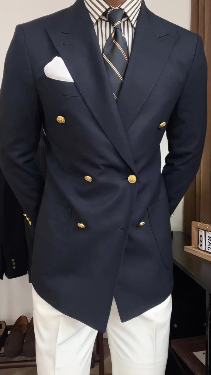 Man wearing a navy double-breasted blazer, striped shirt, tie, and white trousers.