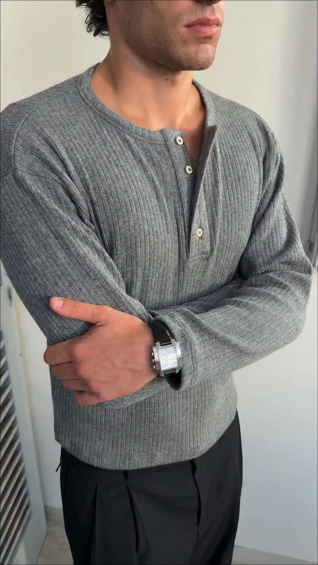 Man wearing a grey ribbed henley shirt, black trousers, and a silver wristwatch.