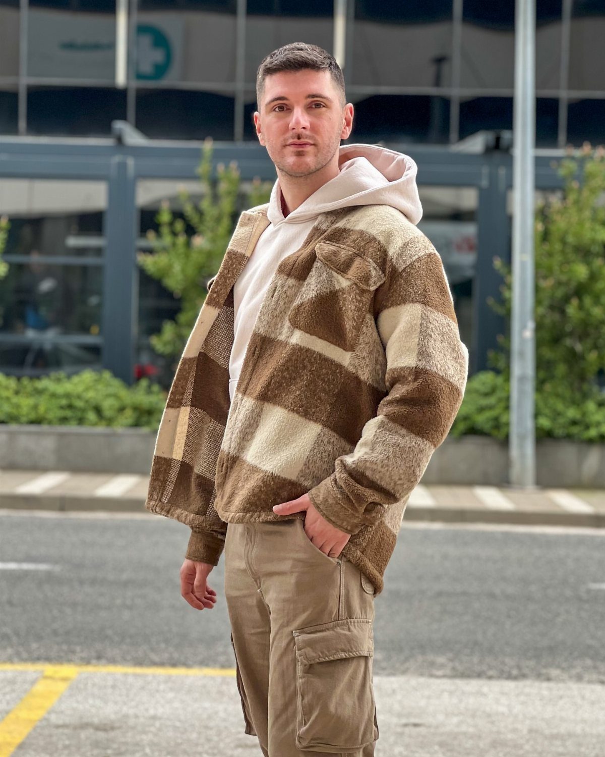 A man wearing a patterned fleece jacket, pink hoodie, and tan cargo pants standing outdoors.