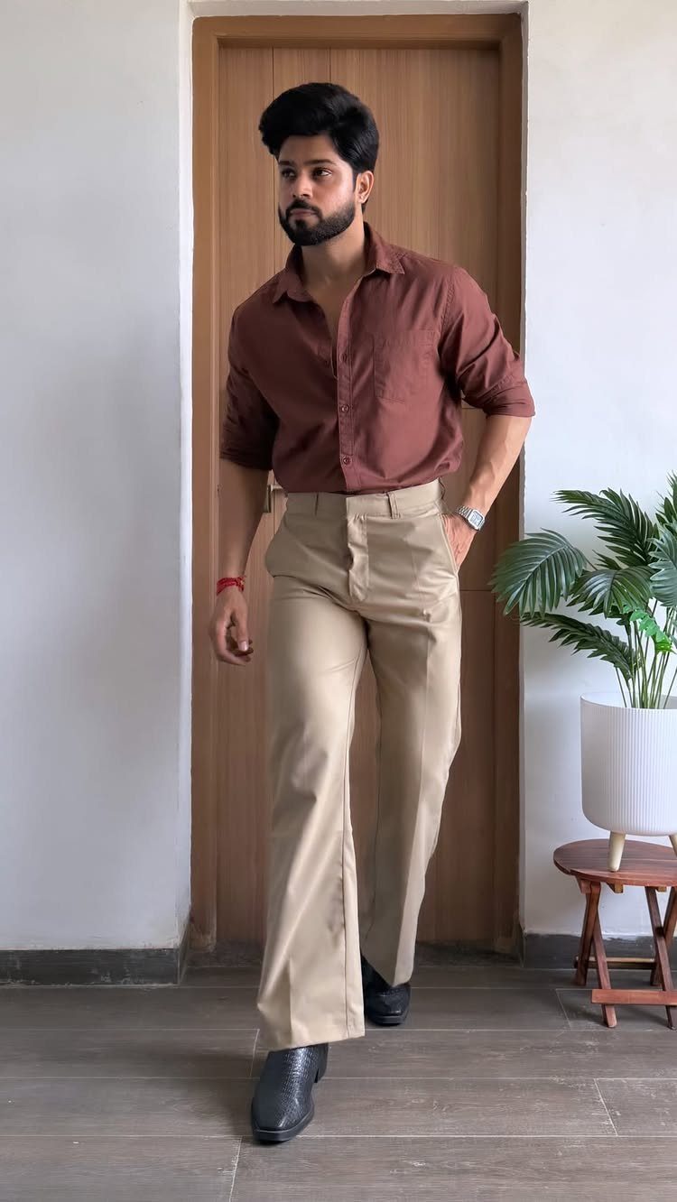 A man wearing a dark reddish-brown shirt and tan trousers standing in a room.