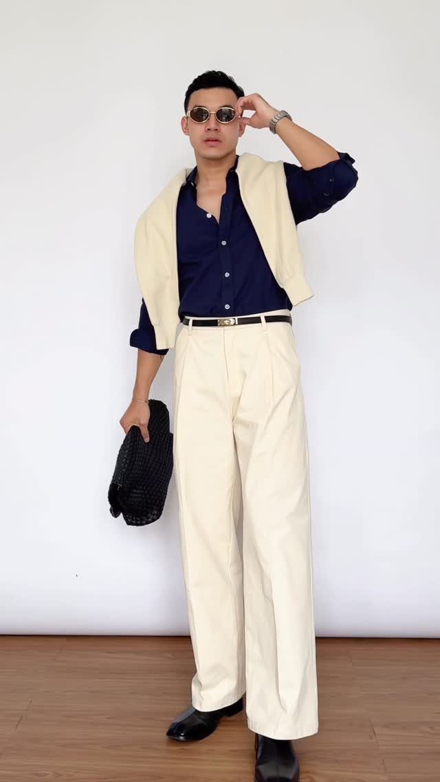 Man wearing a navy blue shirt, cream trousers, cream vest, and black accessories.