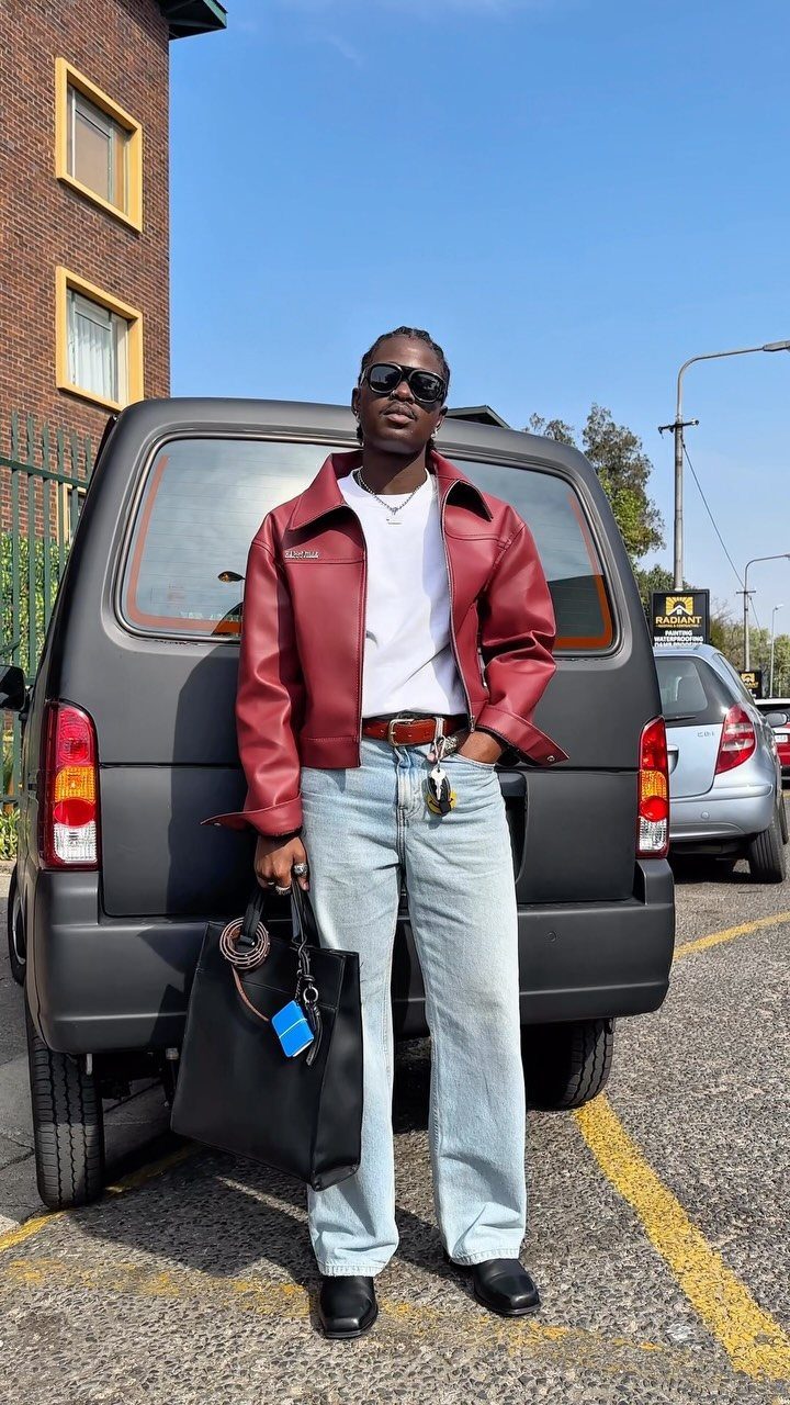 A person posing in a red cropped leather jacket and light blue wide-leg jeans.