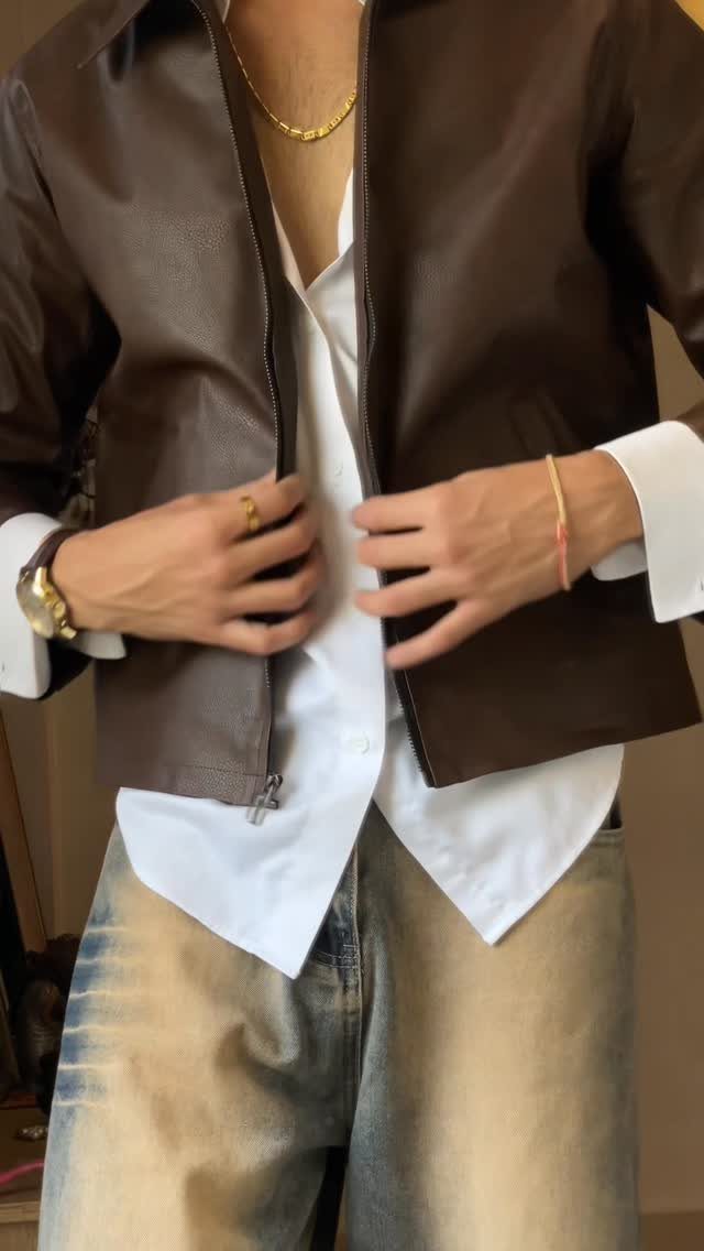 A person wearing a brown cropped leather jacket over a white shirt and light denim jeans.