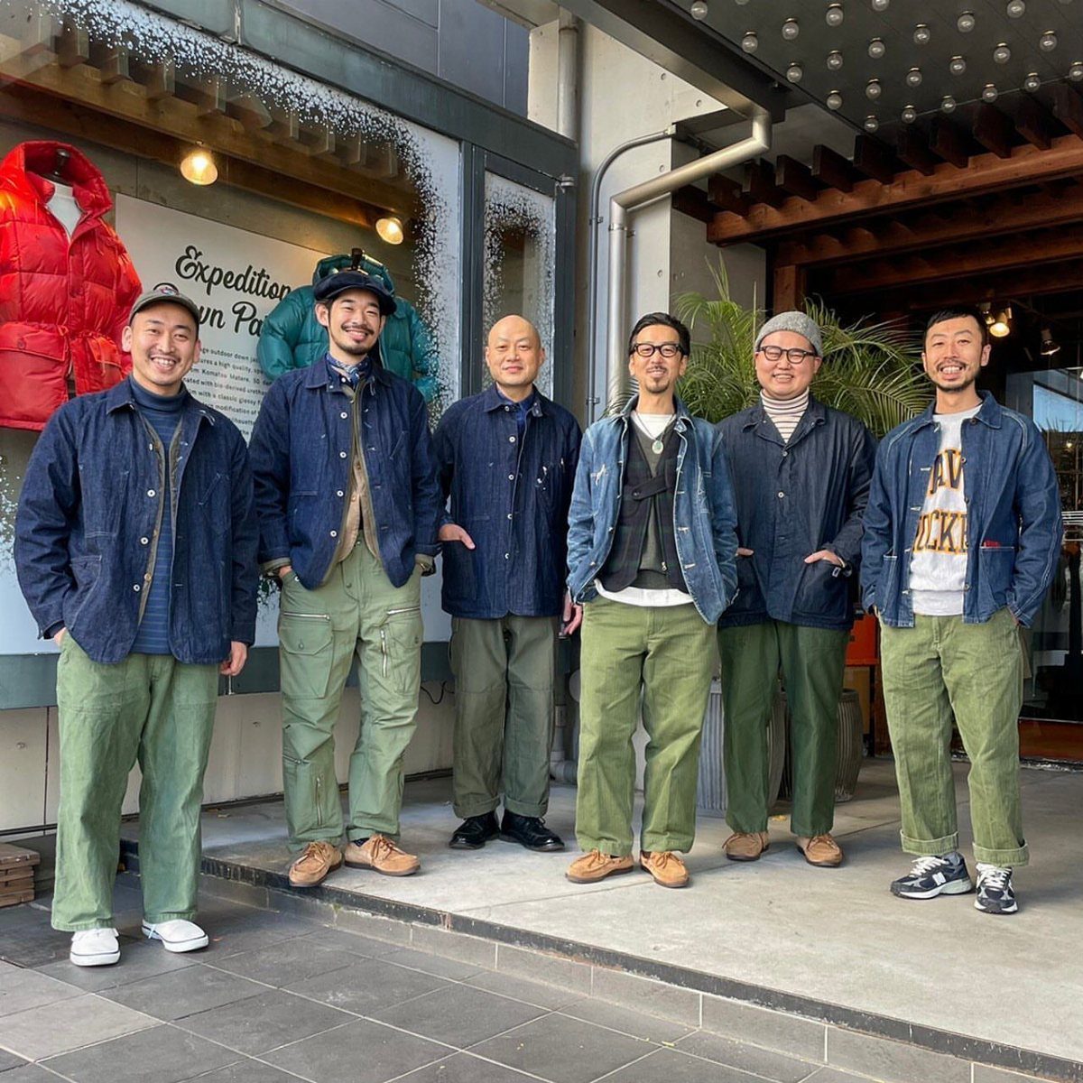 Six men posing together wearing various denim jackets and olive green pants.