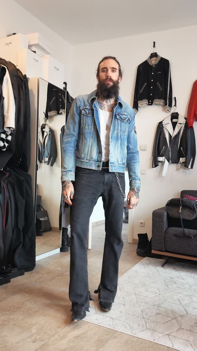 Man with a beard wearing a light blue denim jacket, white t-shirt, and black pants.