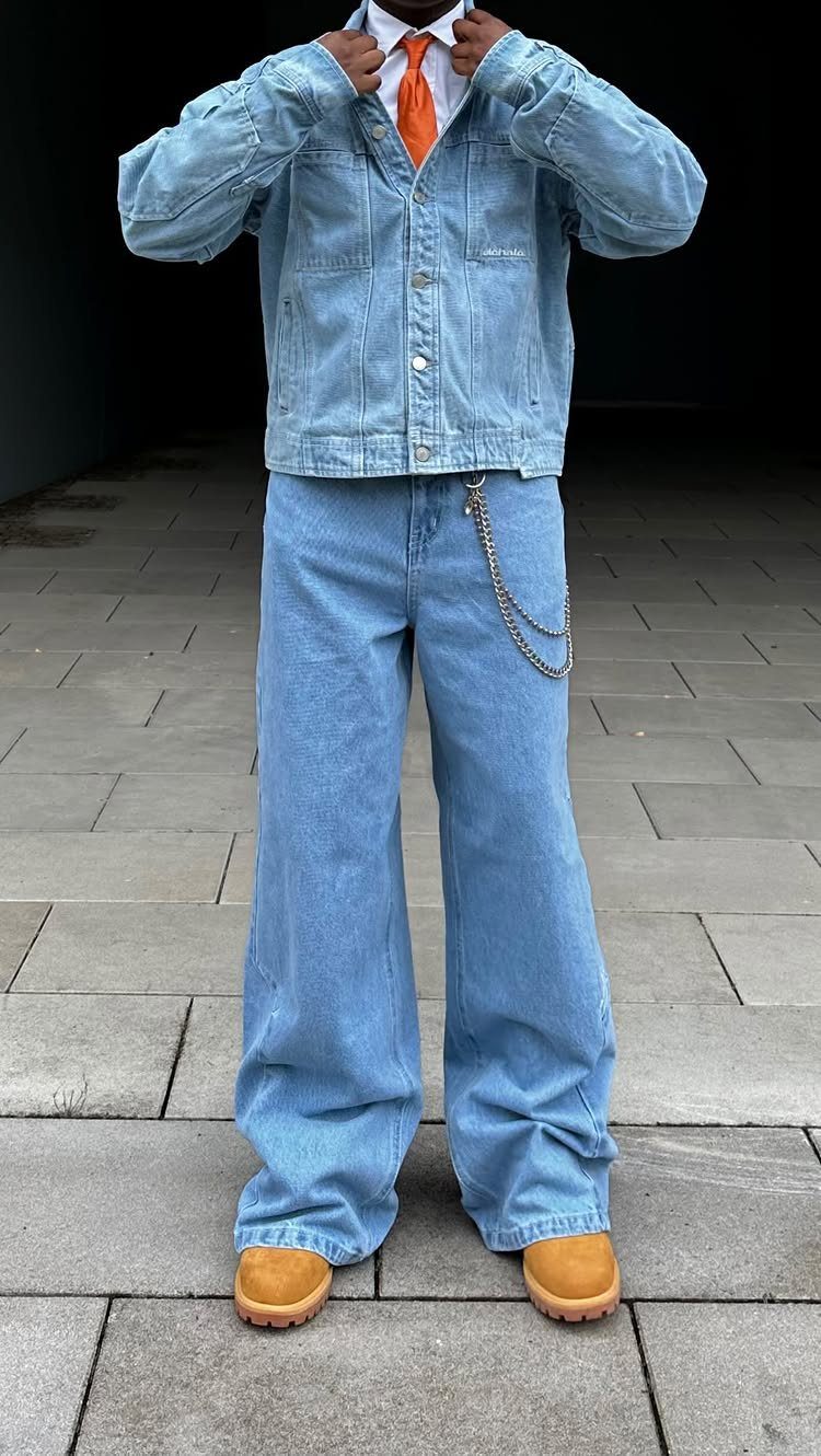 Person wearing a light blue denim jacket, wide-leg denim jeans, an orange tie, and tan boots.