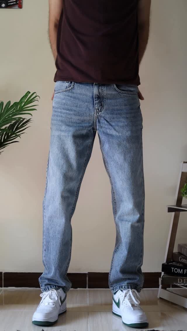 Man wearing light blue relaxed fit denim jeans and white sneakers standing indoors.