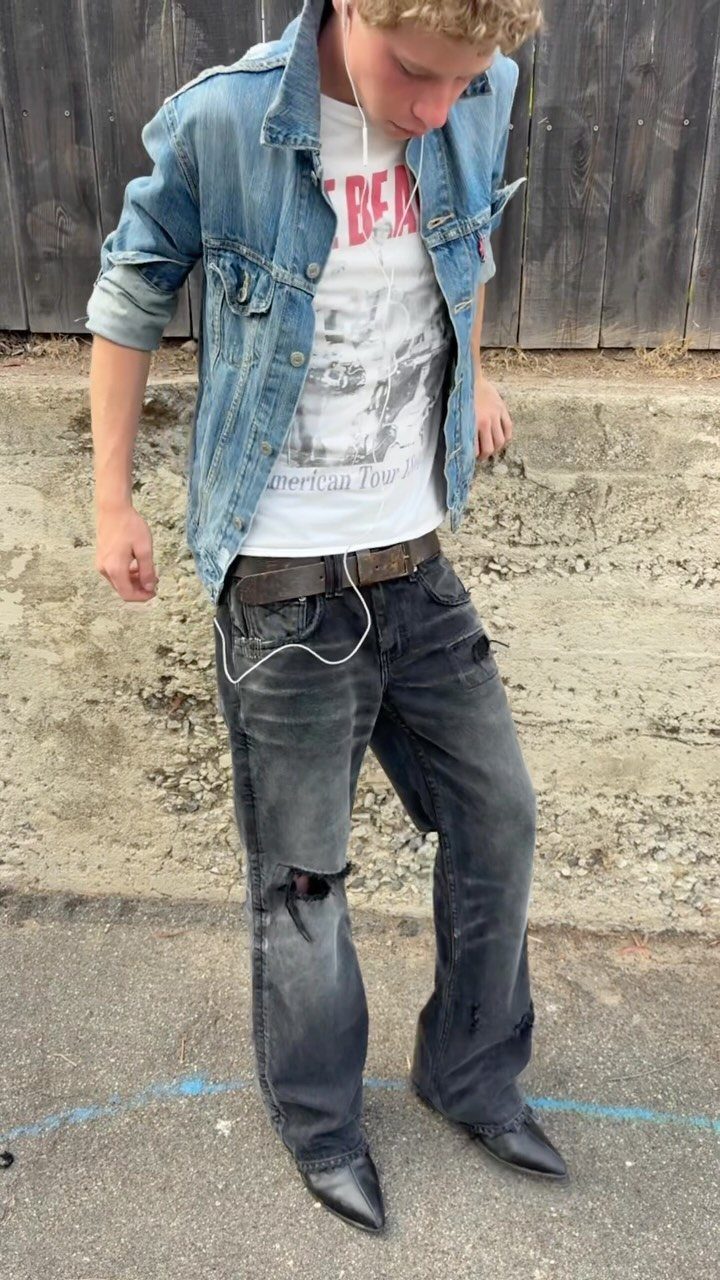 A man wearing a light blue denim jacket, white t-shirt, and dark grey distressed jeans.