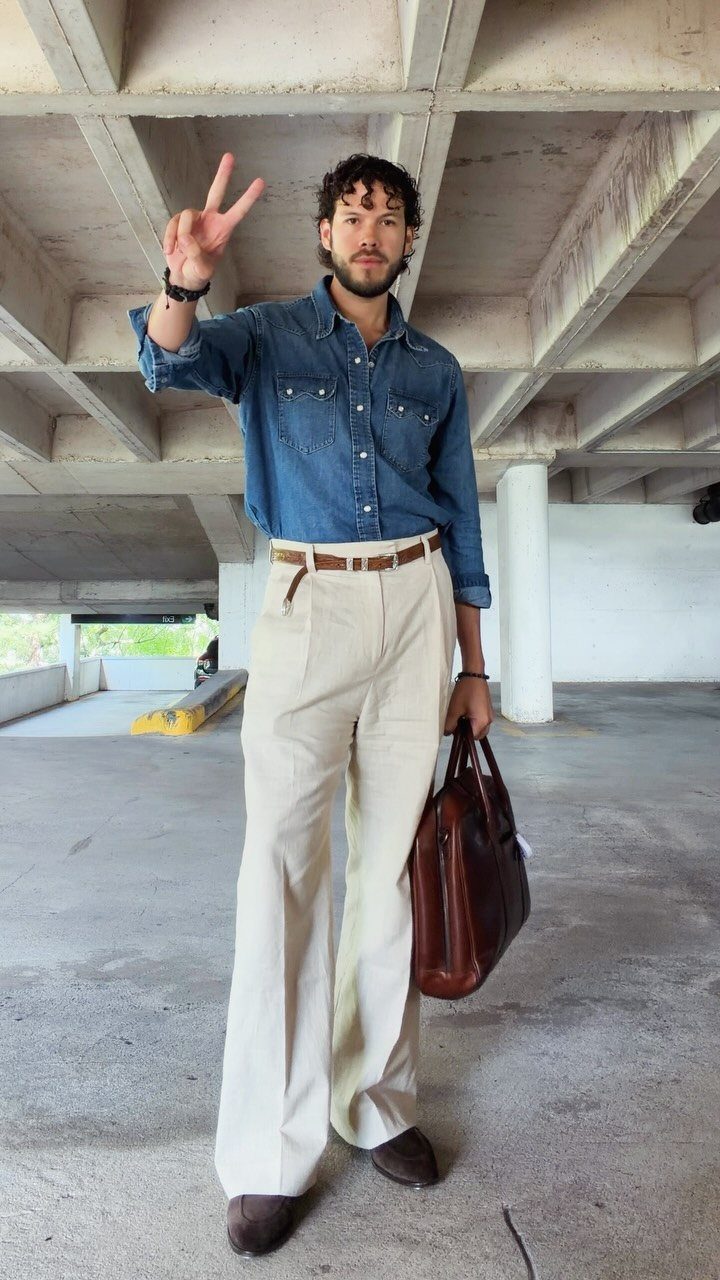 Man in a blue denim snap shirt and cream trousers posing in a parking garage.