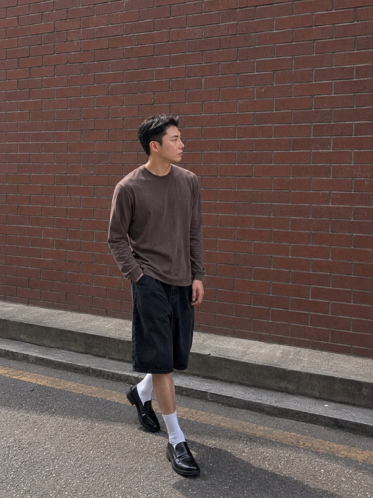 Man walking in black denim shorts, a brown long-sleeve shirt, and black loafers.