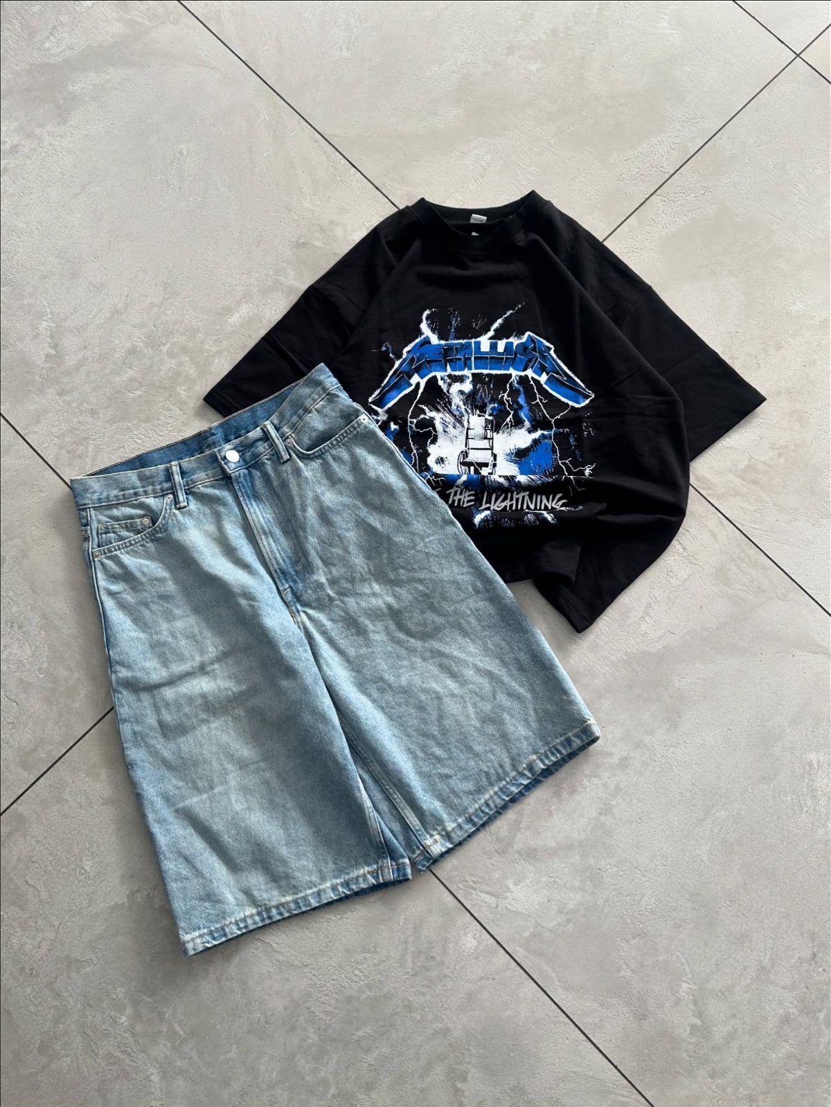 Light blue denim shorts and a black graphic t-shirt laid on grey tiles.