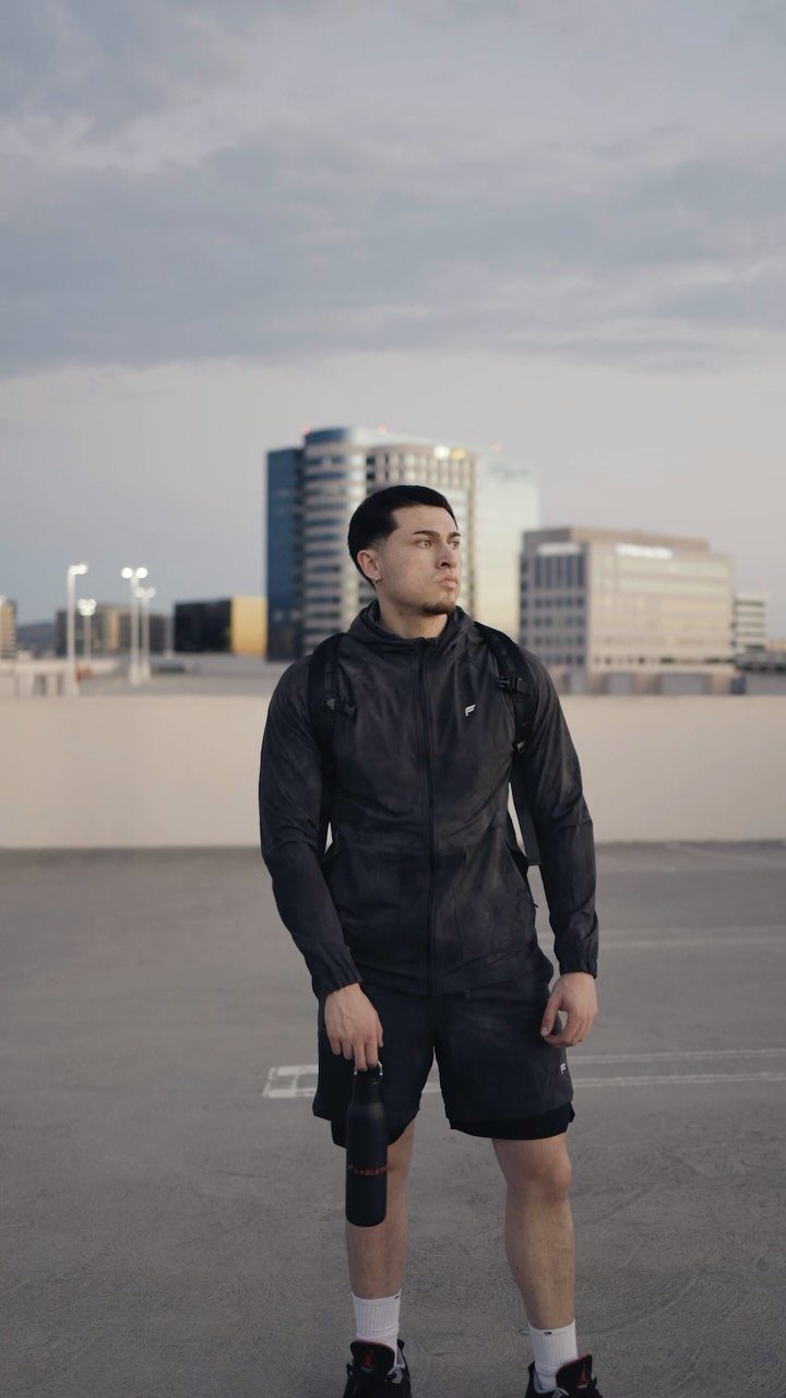 Man in black athletic wear and shorts standing on a rooftop with city buildings behind him.