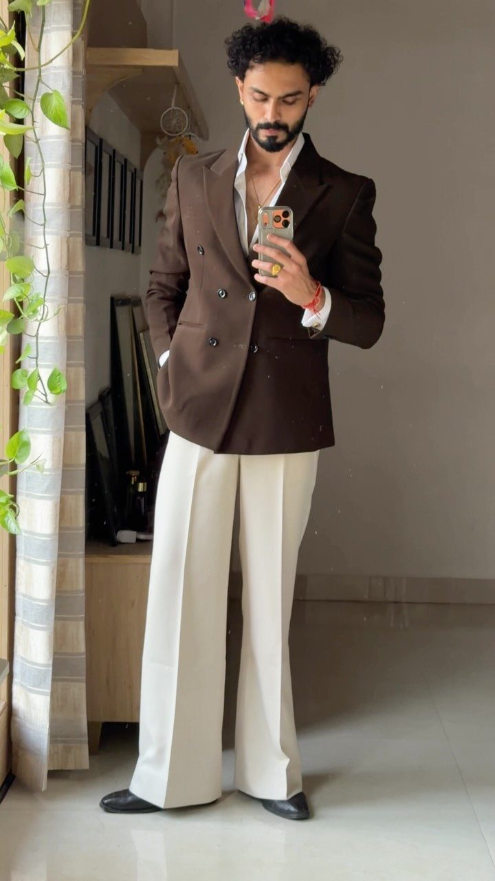 Man in a brown blazer and cream trousers posing for a mirror selfie.