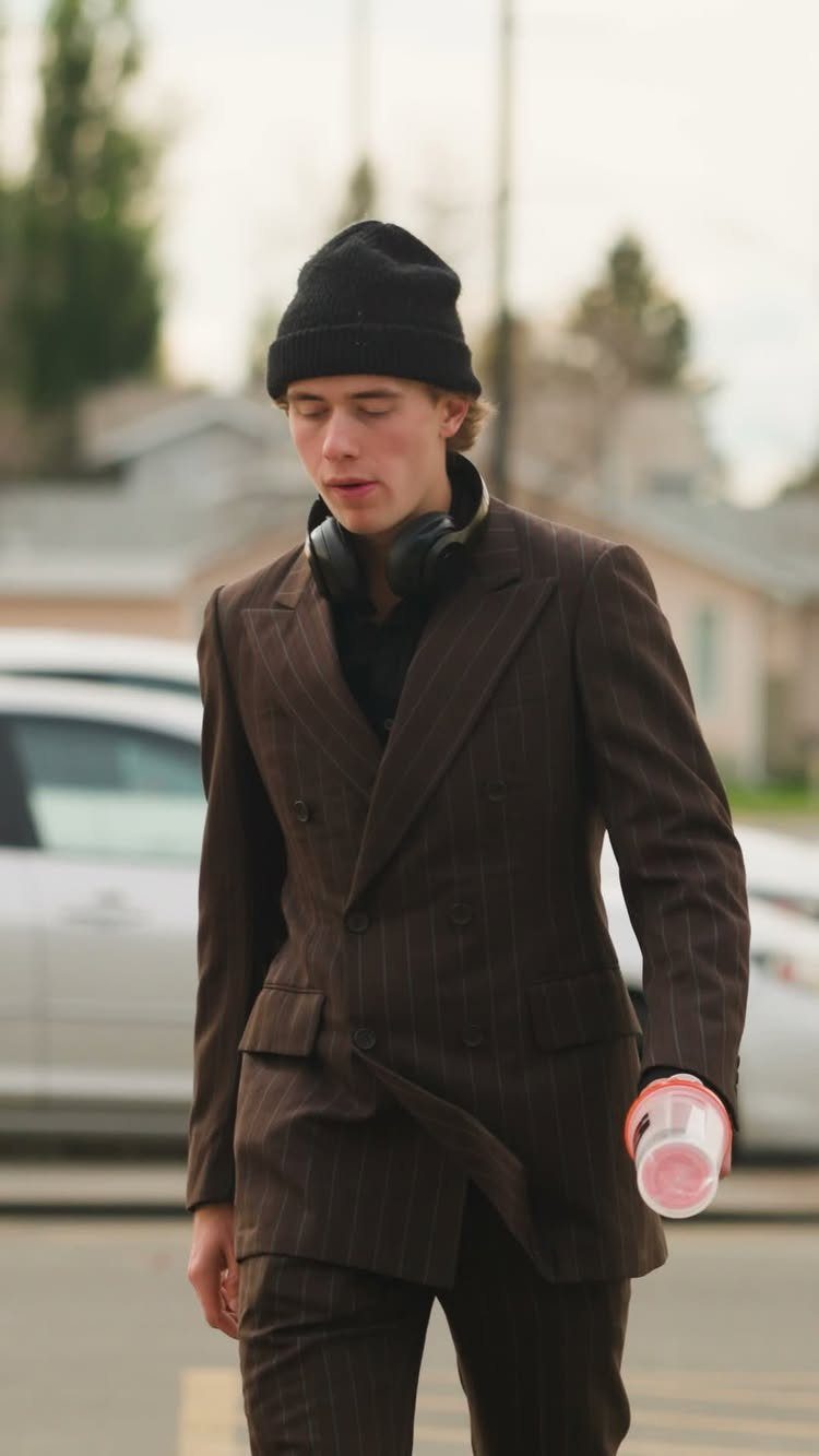 A young man in a brown pinstripe suit wearing a black beanie and headphones.