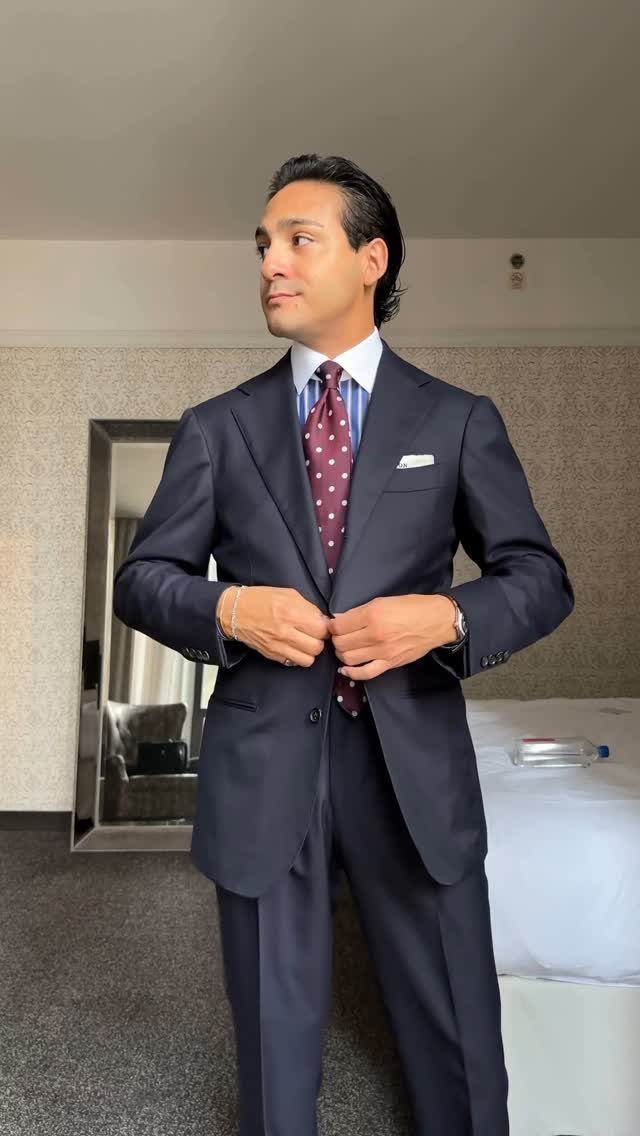 Man in a navy blue business suit and polka-dot tie adjusting his jacket.