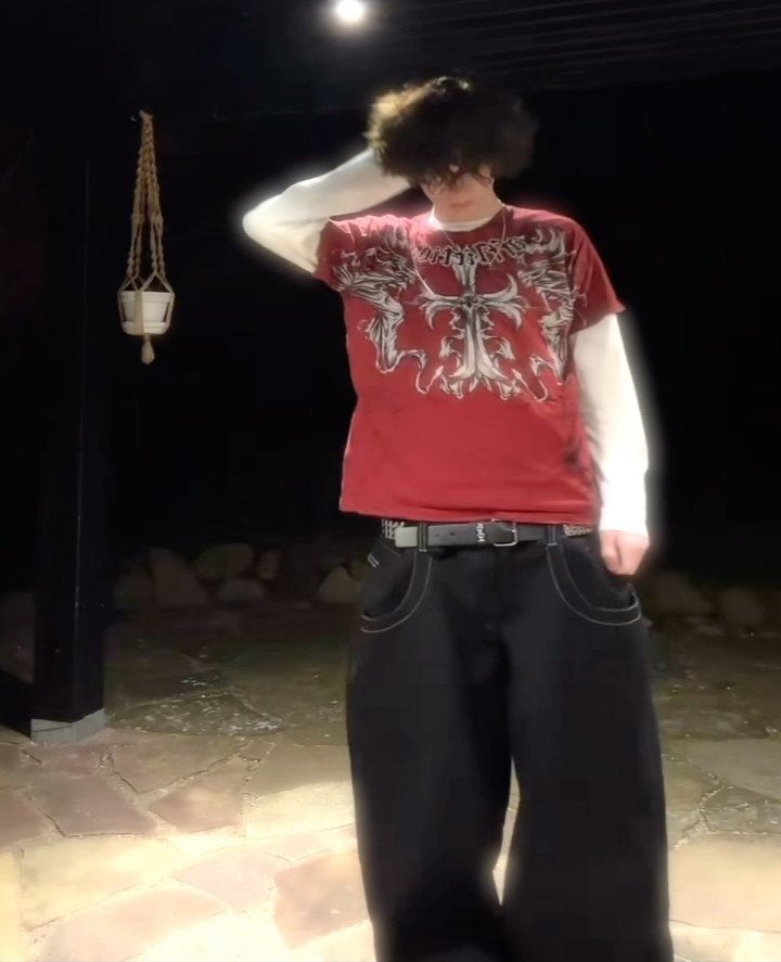 A person wearing a red graphic t-shirt, white long-sleeve undershirt, and baggy black pants.