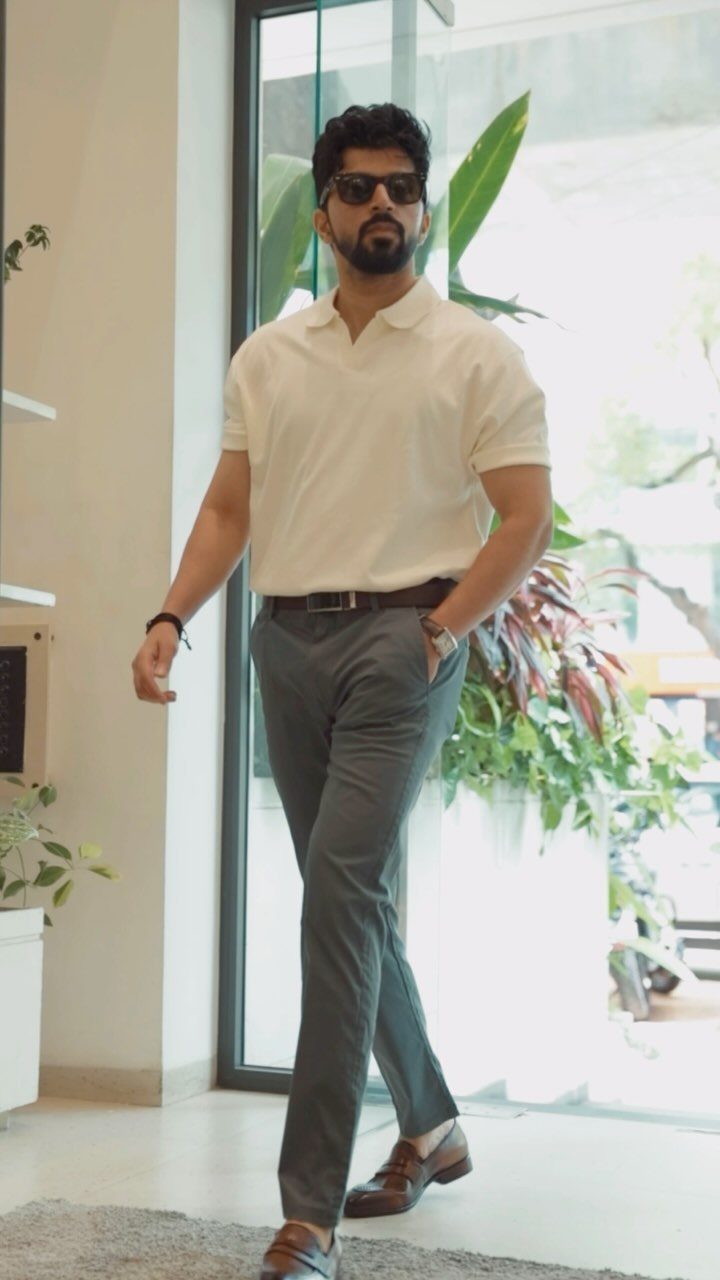 Man walking in a cream polo shirt, grey trousers, and brown loafers outdoors.