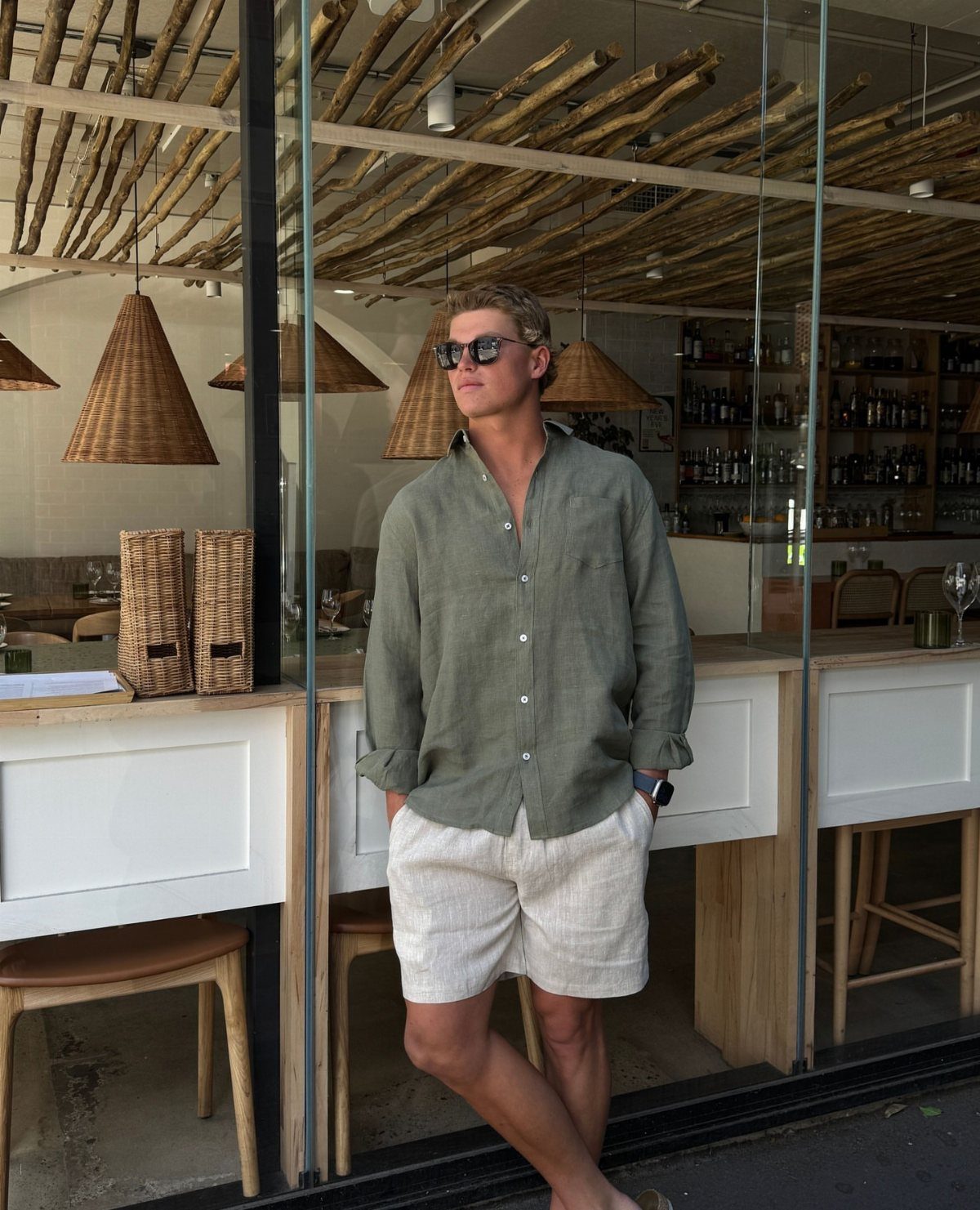 Man in olive linen shirt and white linen shorts standing outside a restaurant.