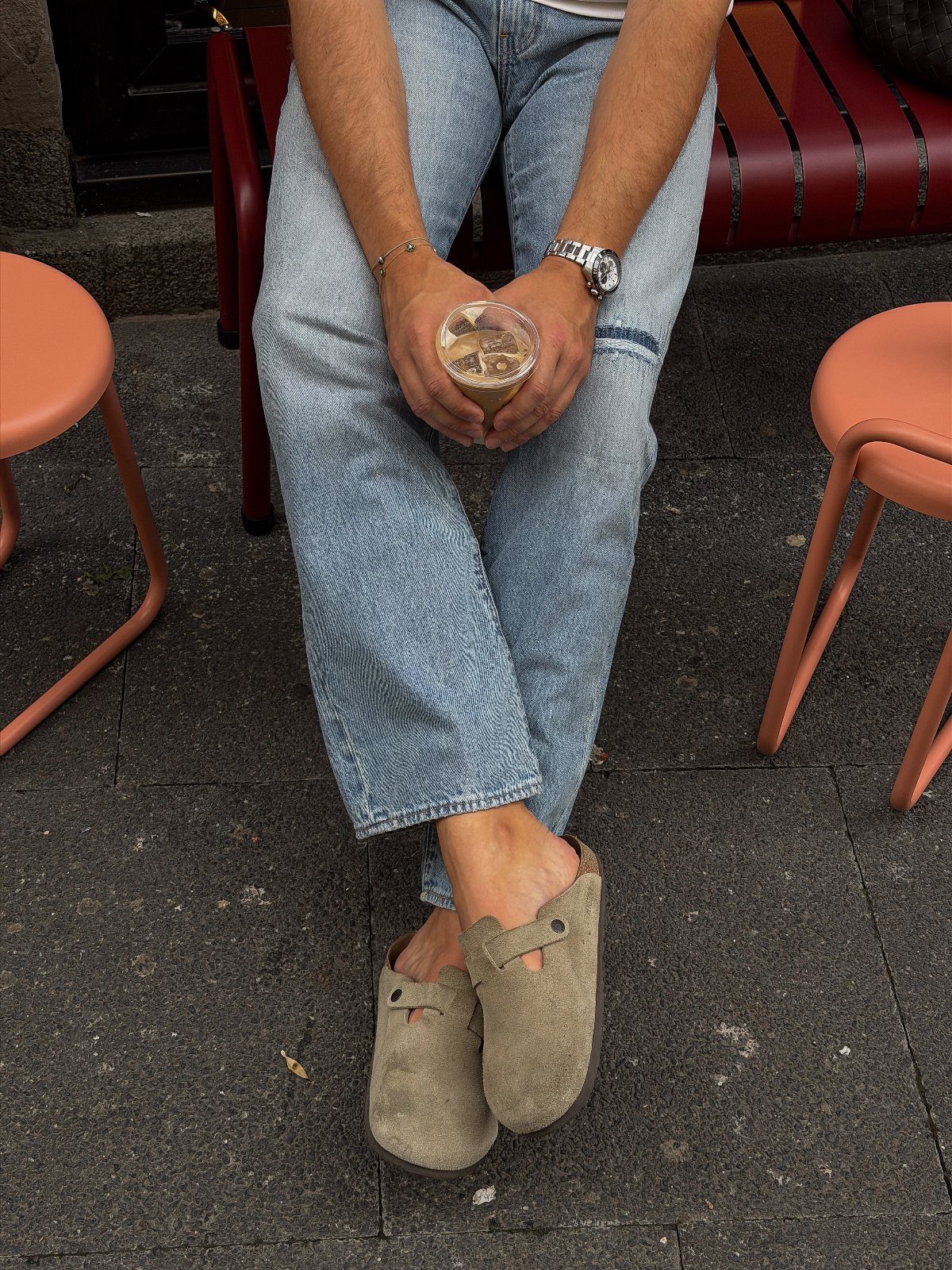 Person wearing patterned blue jeans and tan suede slip-on loafers while sitting outdoors.