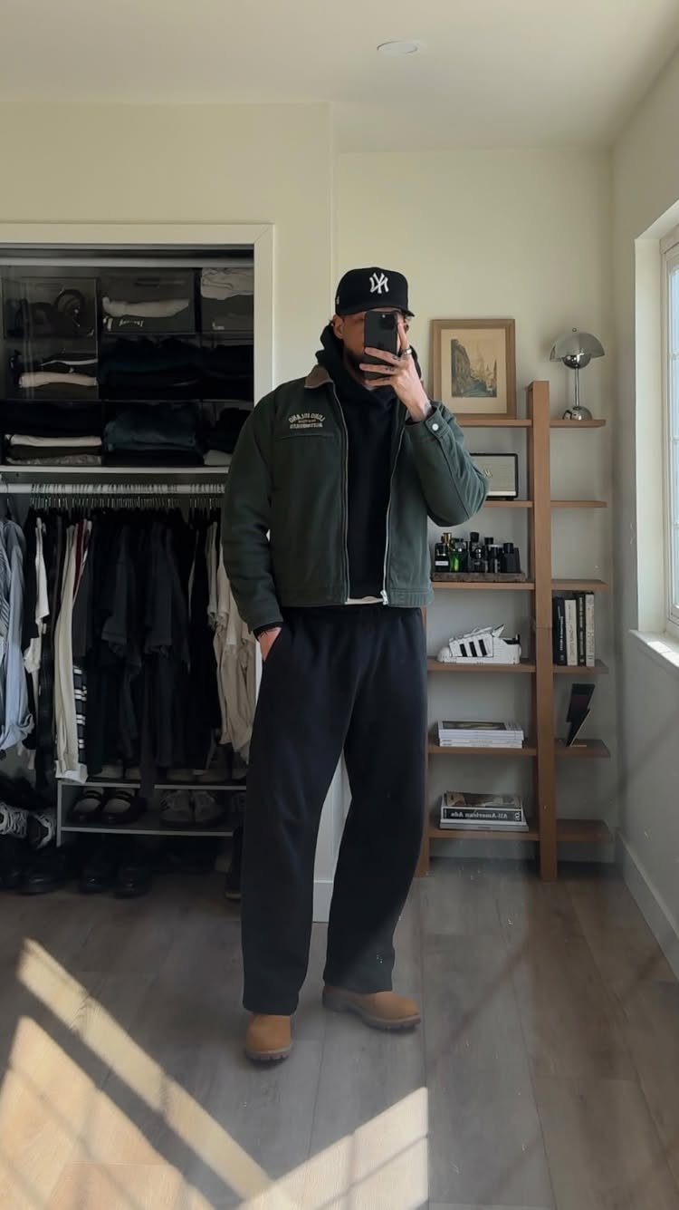 Man in a green bomber jacket, black hoodie, and baggy sweatpants posing for a mirror selfie.