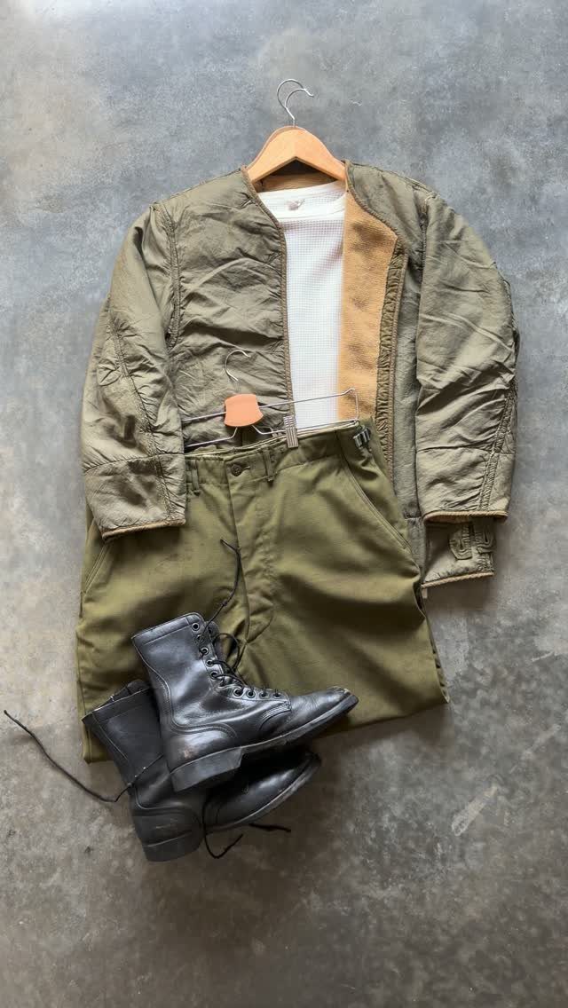 Black leather combat boots paired with an olive green jacket and shorts on concrete.
