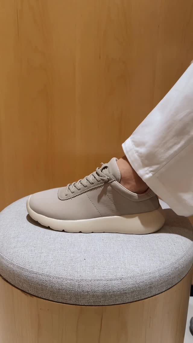 A beige sneaker sits on a grey round stool against a wooden wall.