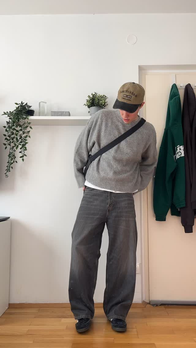 A person wearing a grey cozy sweater and baggy dark grey pants with a crossbody bag.