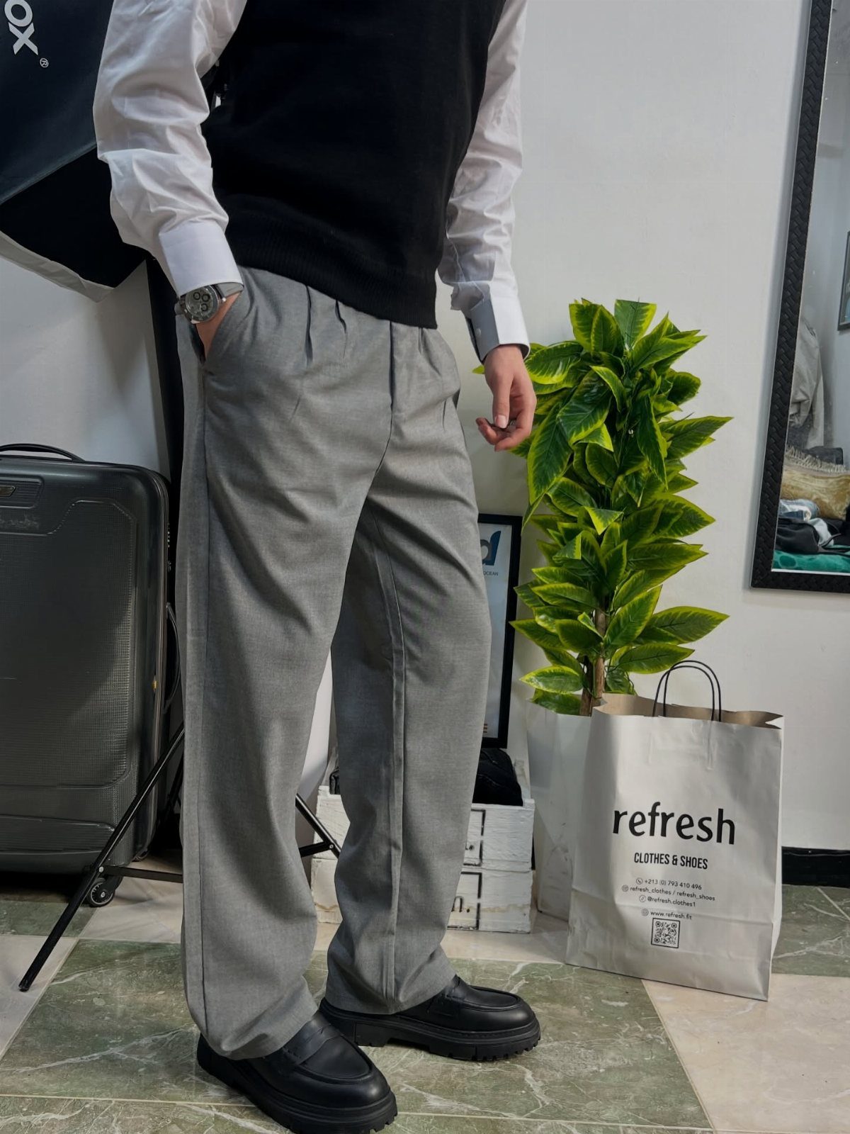 Person wearing grey trousers paired with black chunky loafers and a black sweater vest.