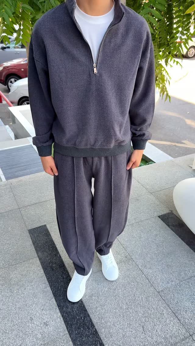 A person wearing a charcoal grey quarter-zip sweater and matching sweatpants with white sneakers.