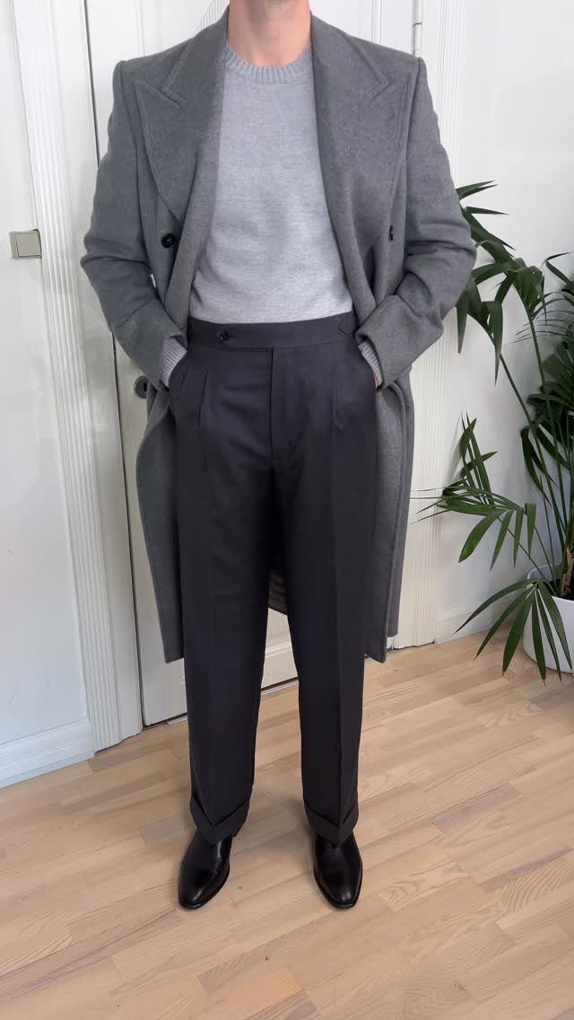Man wearing a grey sweater, long overcoat, dark trousers, and black leather boots.