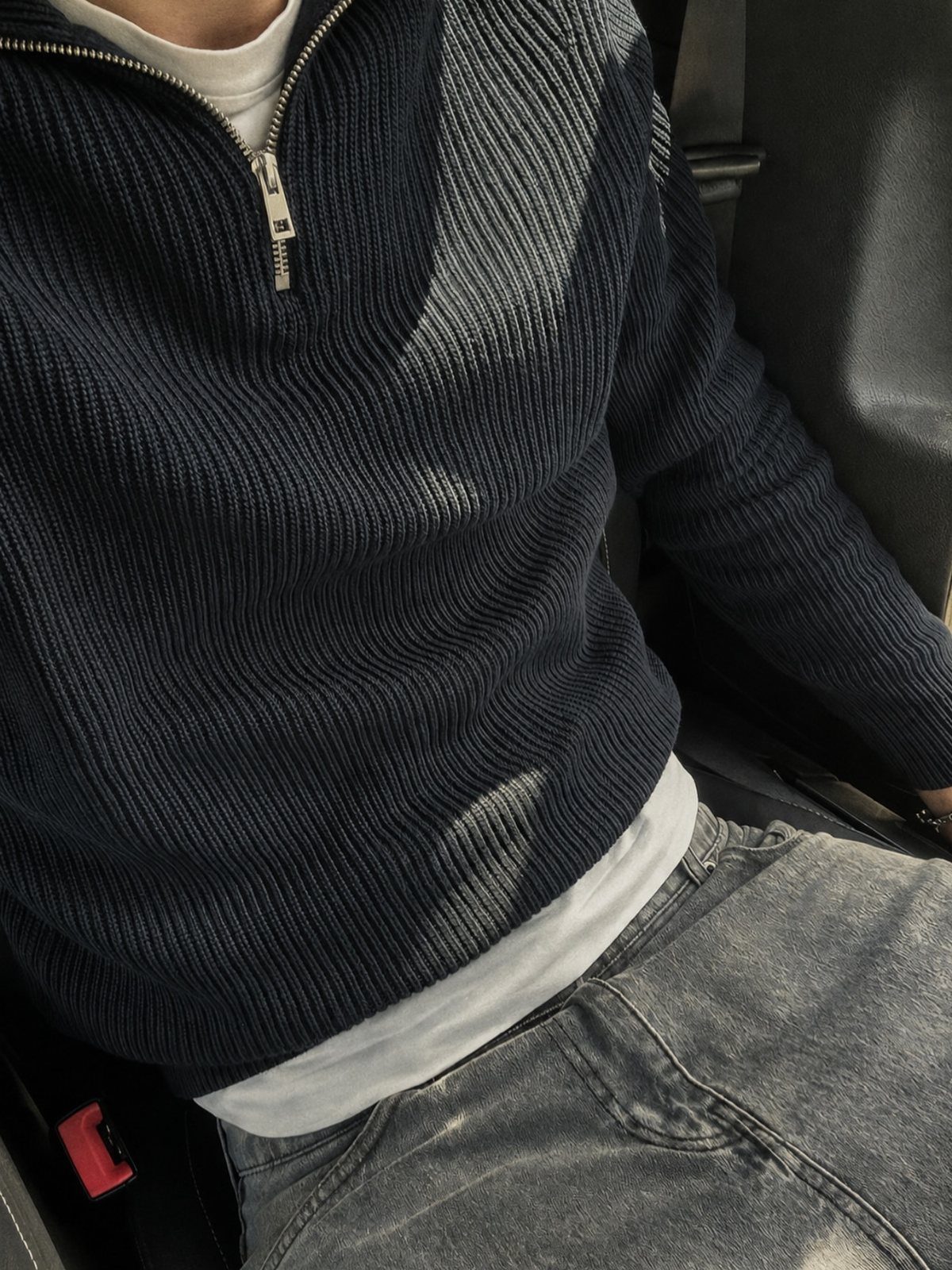 Person wearing a dark grey ribbed quarter-zip sweater and grey denim jeans.