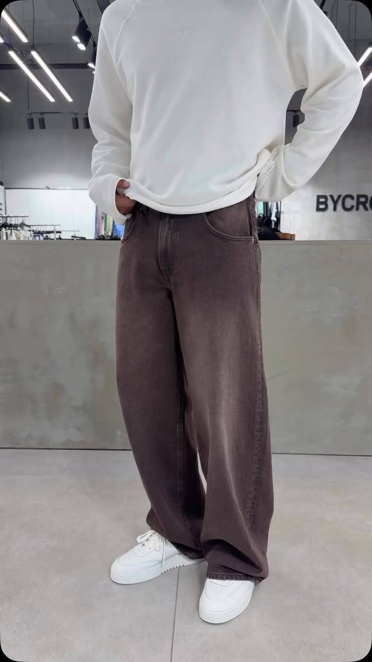 A person wearing a white sweatshirt, baggy brown denim jeans, and white sneakers.