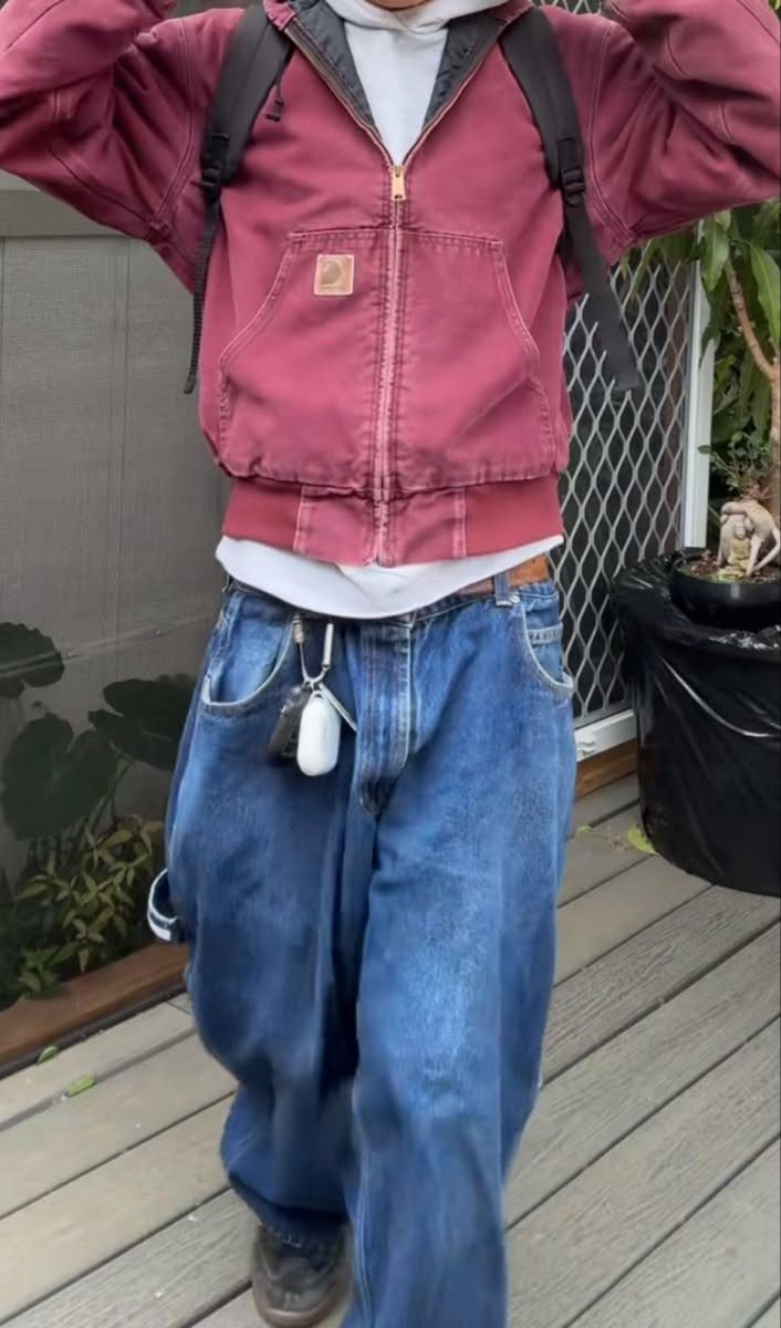 A person wearing a maroon cropped jacket over a white hoodie and baggy blue jeans.