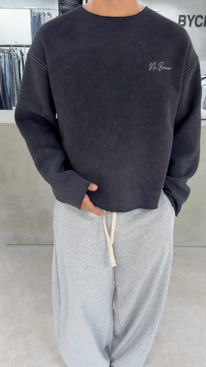 Man wearing a black oversized sweatshirt and grey sweatpants in a clothing store.