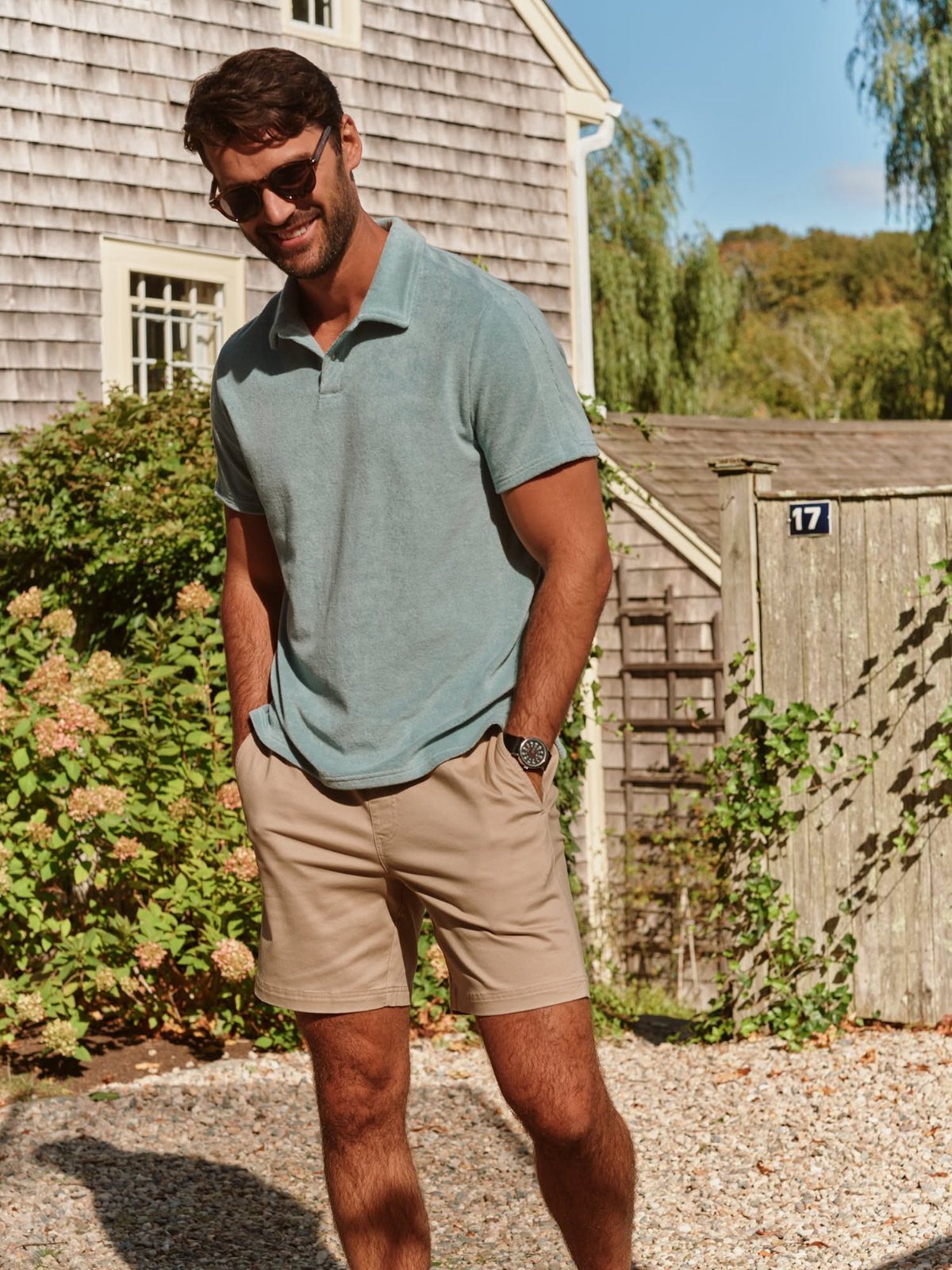 A man in a light blue polo shirt and beige shorts smiling outdoors.