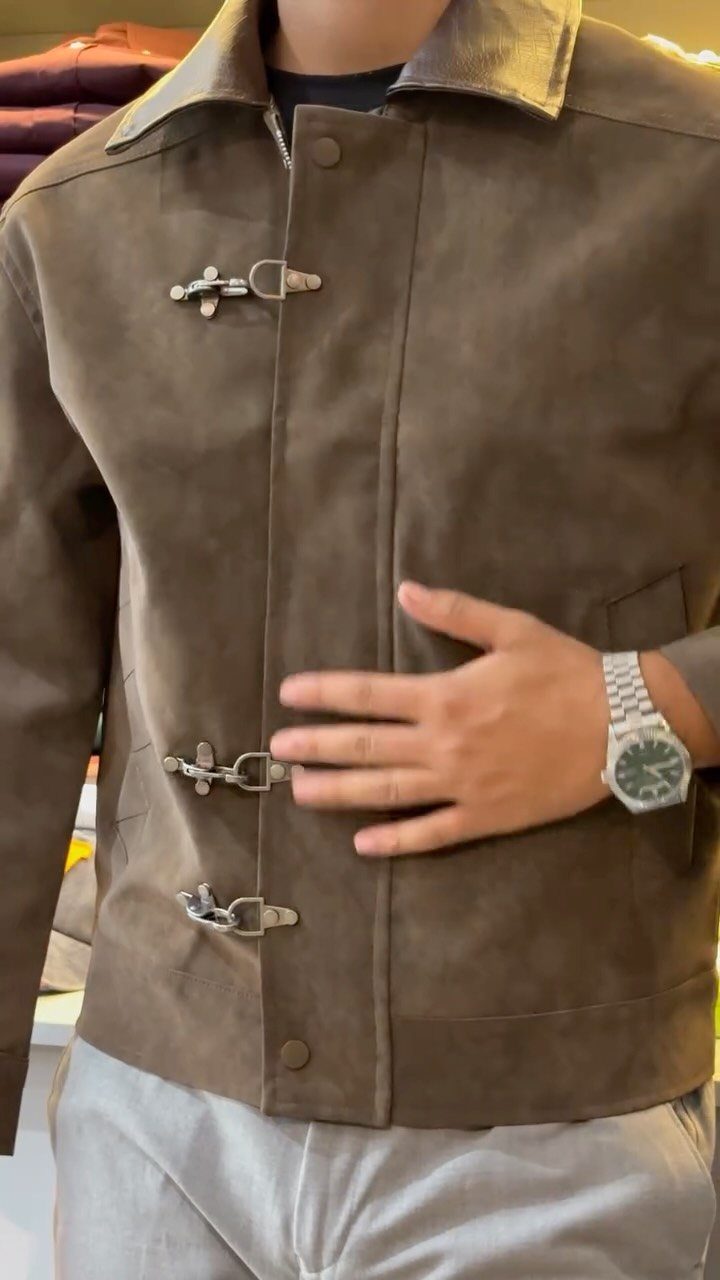 A person wearing a brown suede jacket with silver toggle closures and a leather collar.