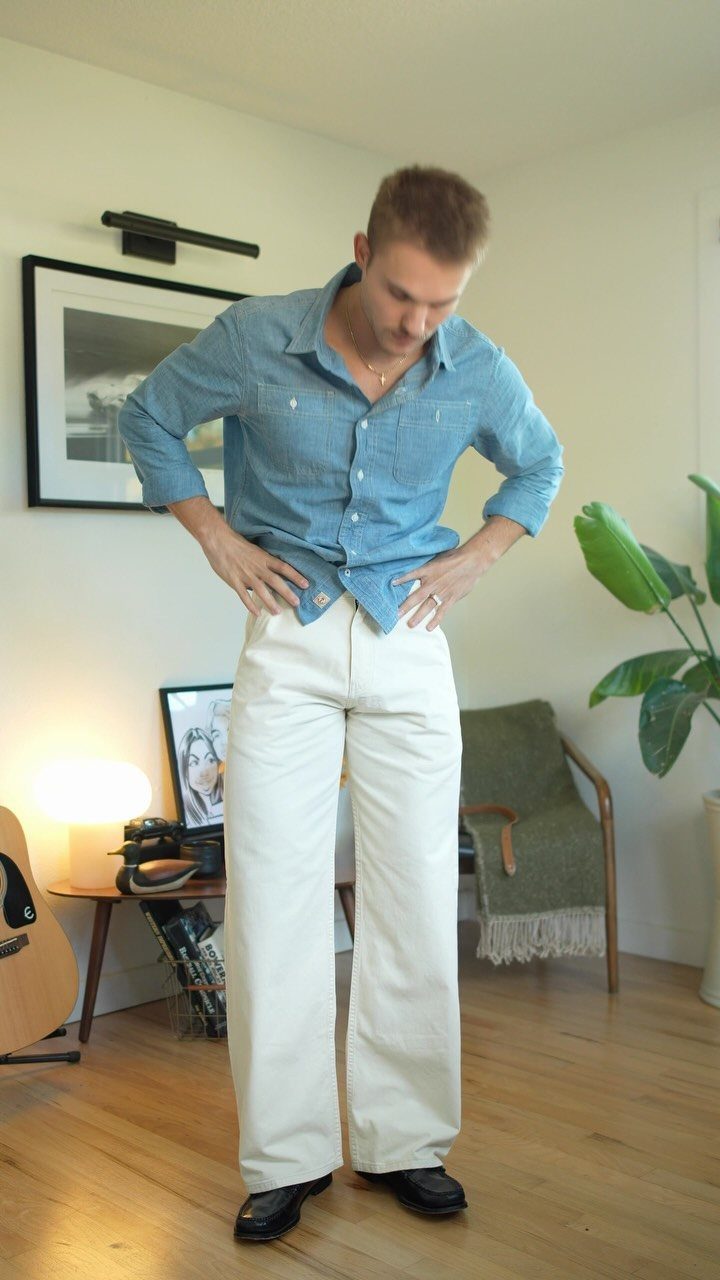 Man wearing a light blue denim shirt and wide-leg cream trousers with black loafers.