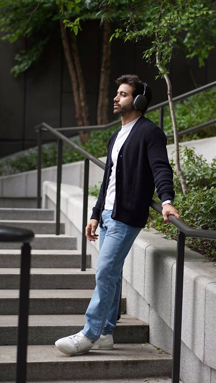 A man in a white t-shirt, navy cardigan, and light blue jeans standing on stairs.