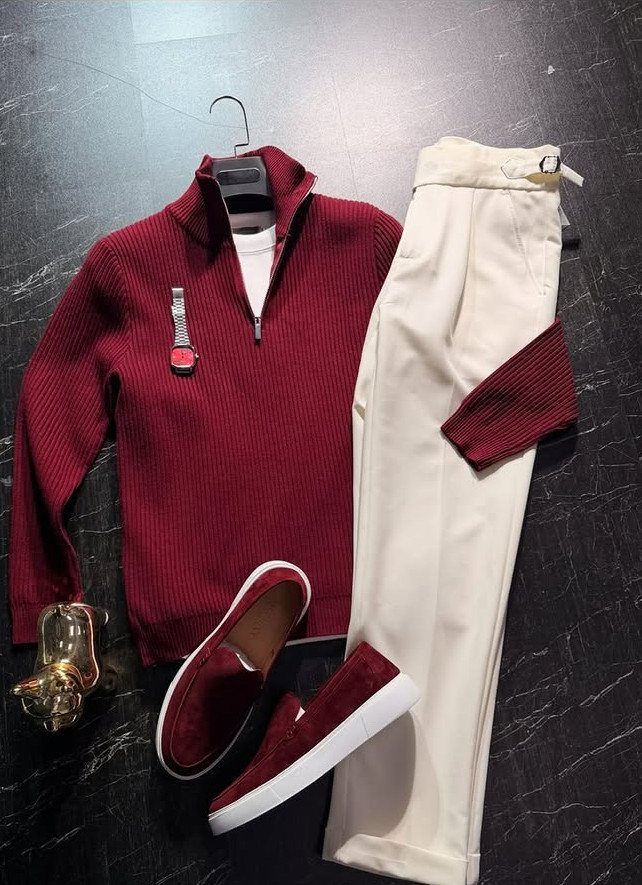 Burgundy ribbed sweater, white trousers, and burgundy loafers arranged on a dark marble surface.