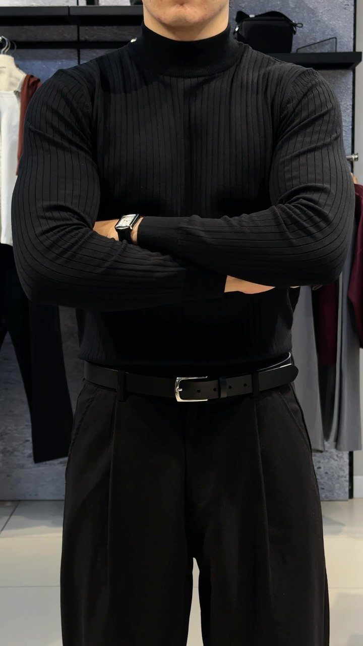 Man in a black ribbed turtleneck, black trousers, and a black leather belt.