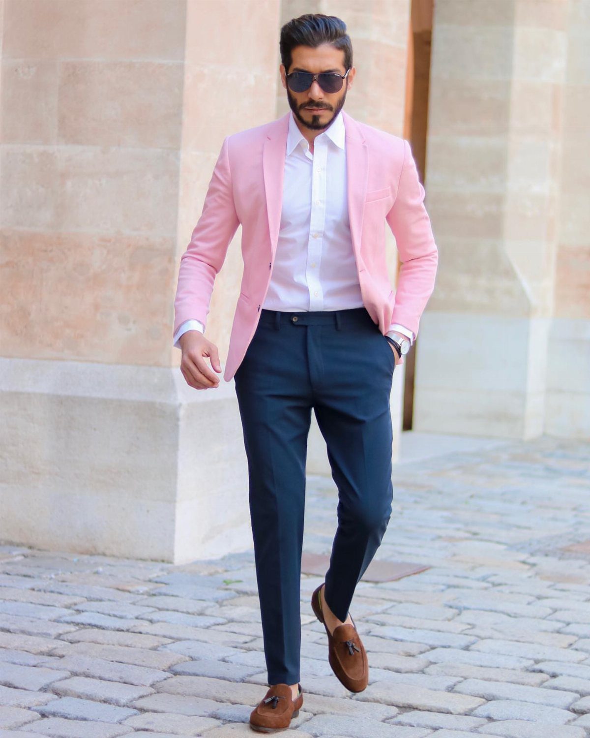 Man in a pink blazer, white shirt, and navy trousers walking on a cobblestone street.