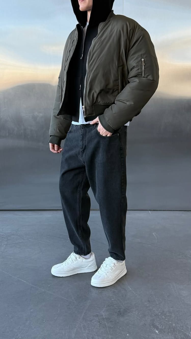 Man wearing an olive green bomber jacket, black hoodie, black jeans, and white sneakers.