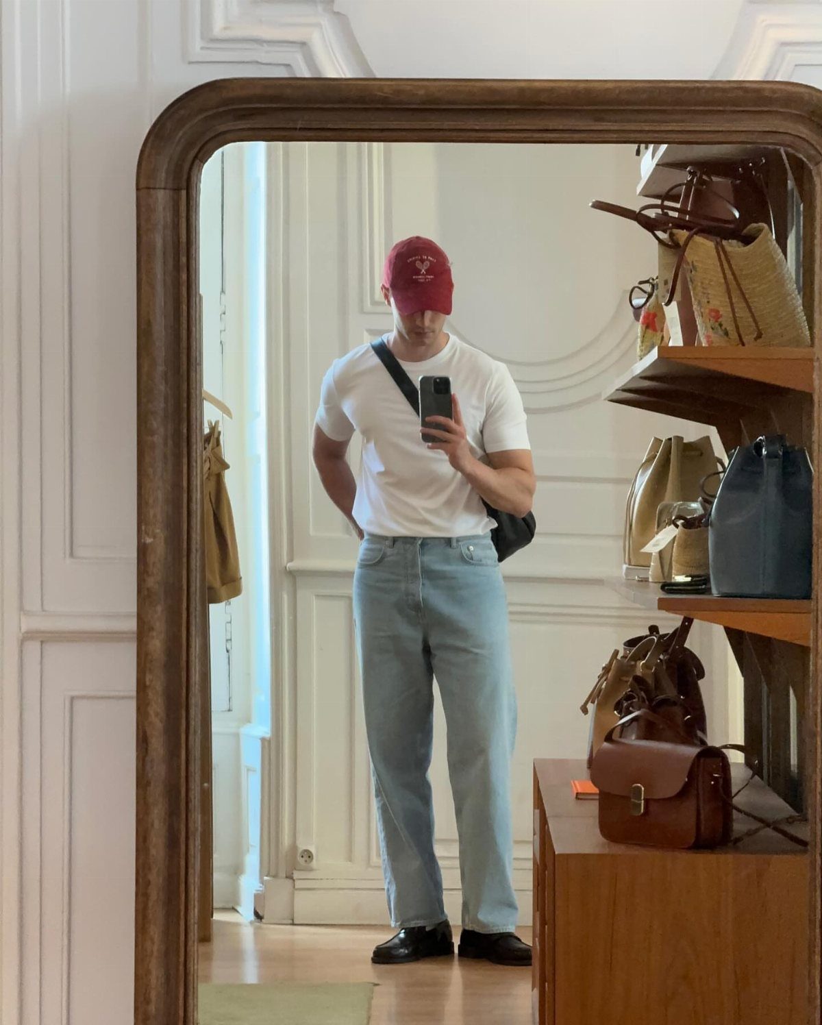 Man in white t-shirt and light blue jeans wearing black casual loafers taking a mirror selfie.